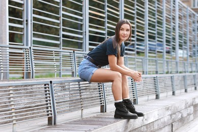 Photo of Beautiful woman in stylish denim shorts sitting on metal bench backrest outdoors