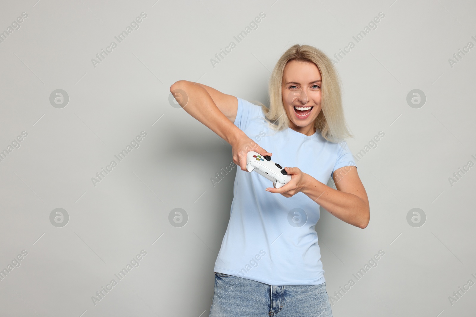 Photo of Happy woman playing video games with controller on gray background, space for text