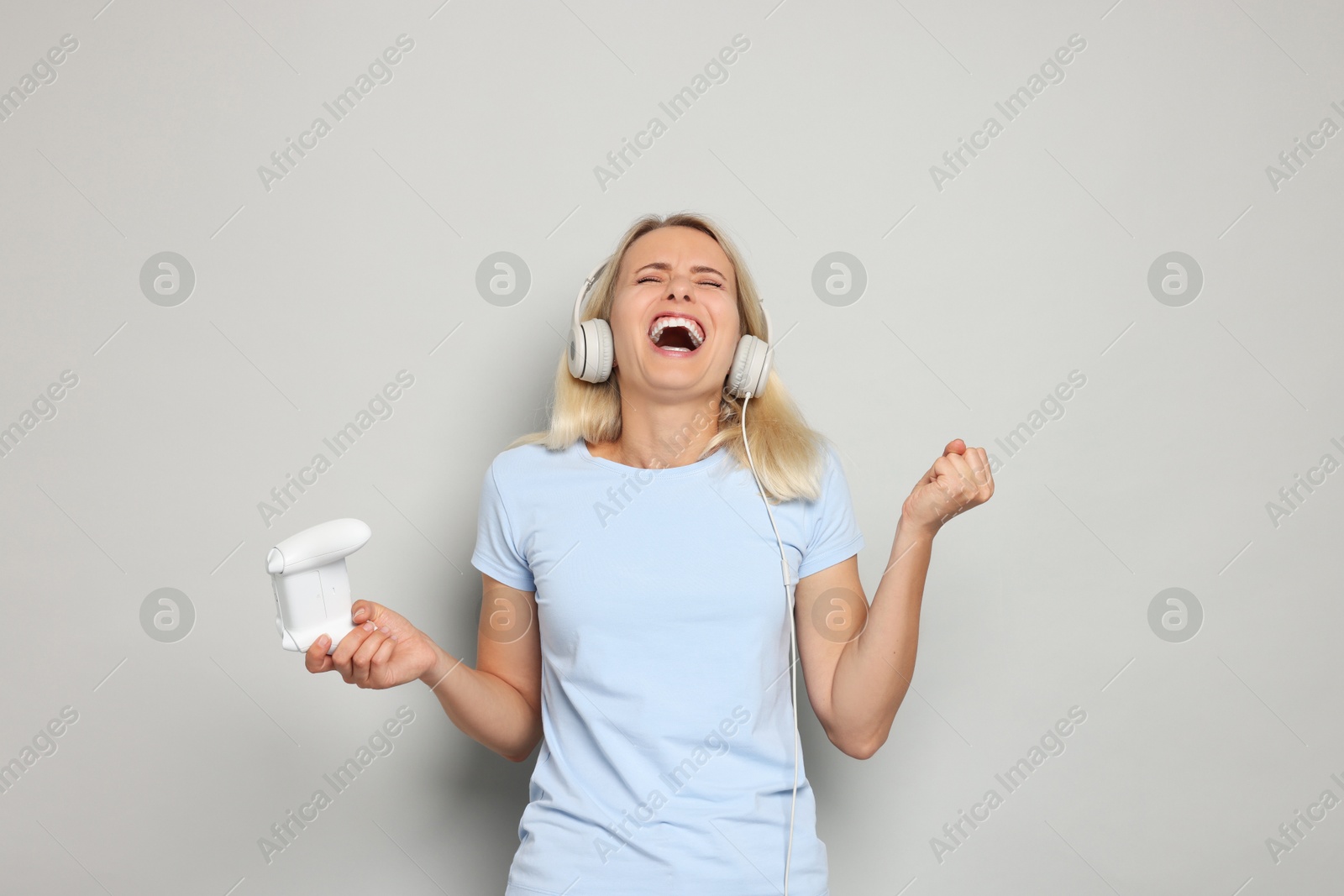 Photo of Emotional woman in headphones with controller on gray background