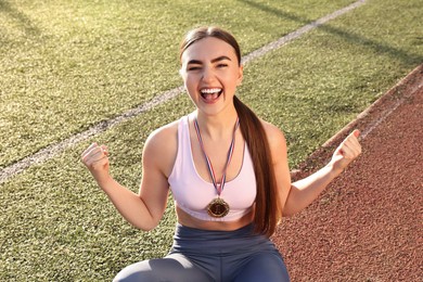 Happy winner with golden medal sitting at stadium on sunny day