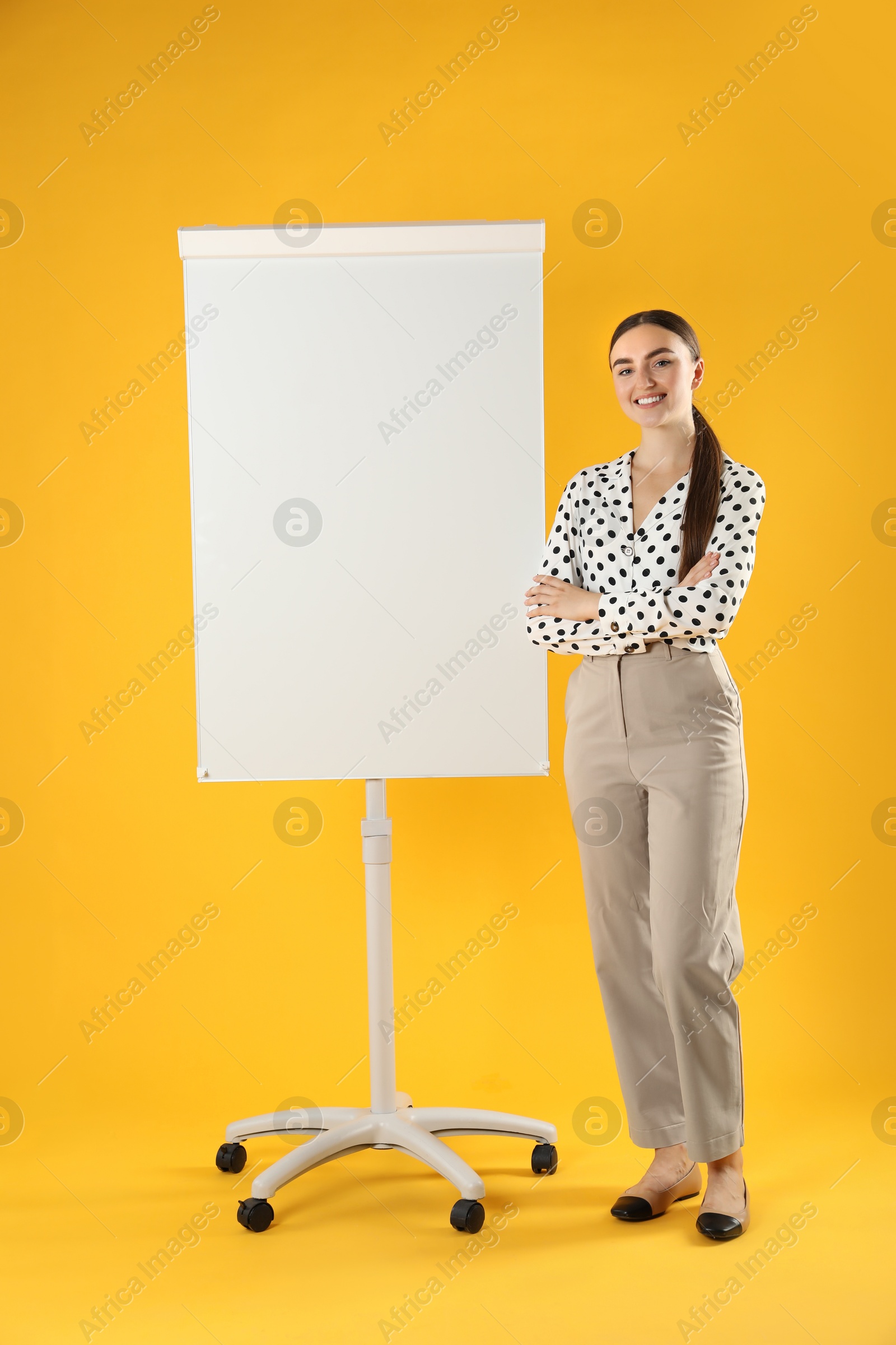 Photo of Happy woman near flip chart on orange background. Mockup for design