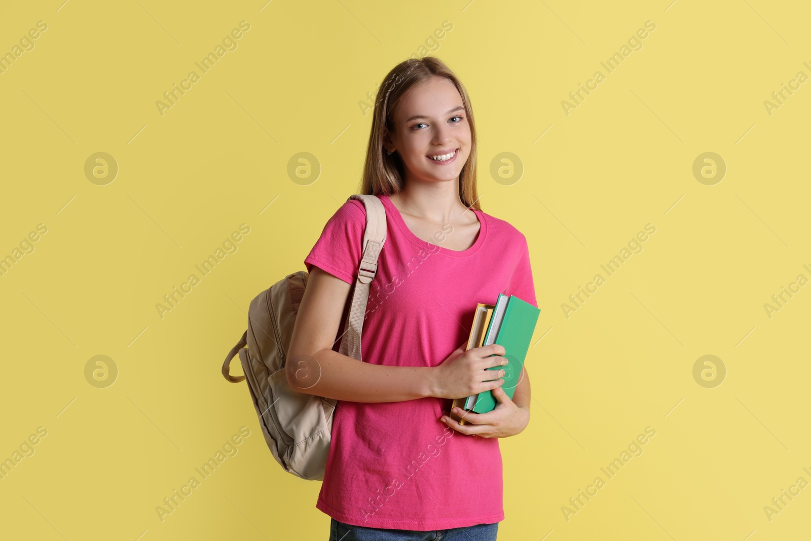 Photo of Teenage girl with books and backpack on yellow background