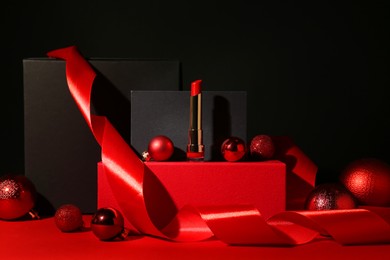 Photo of Christmas present. Red lipstick, boxes and festive decor against black background