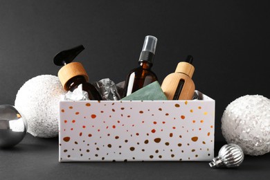 Photo of Cosmetic products in box as Christmas gift and festive balls on black background