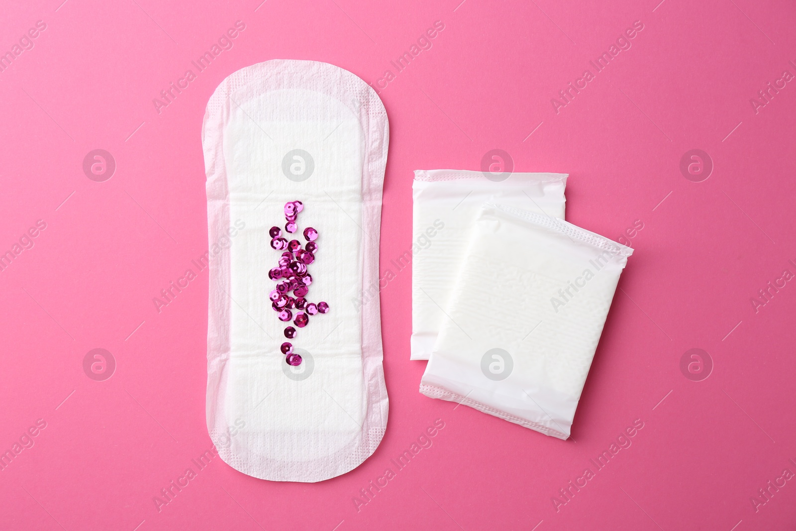 Photo of Menstrual pads and sequins on pink background, top view