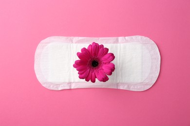 Photo of Menstrual pad with flower on pink background, top view