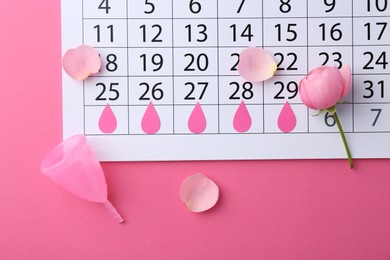 Photo of Flat lay composition with calendar and menstrual cup on pink background