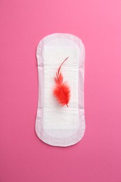 Photo of Menstrual pad with red feather on pink background, top view