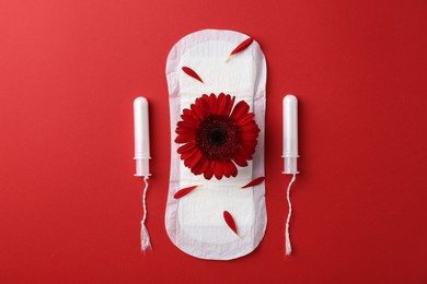 Photo of Menstrual pad with flower and tampons on red background, flat lay