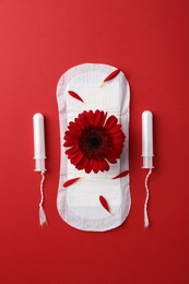 Menstrual pad with flower and tampons on red background, flat lay