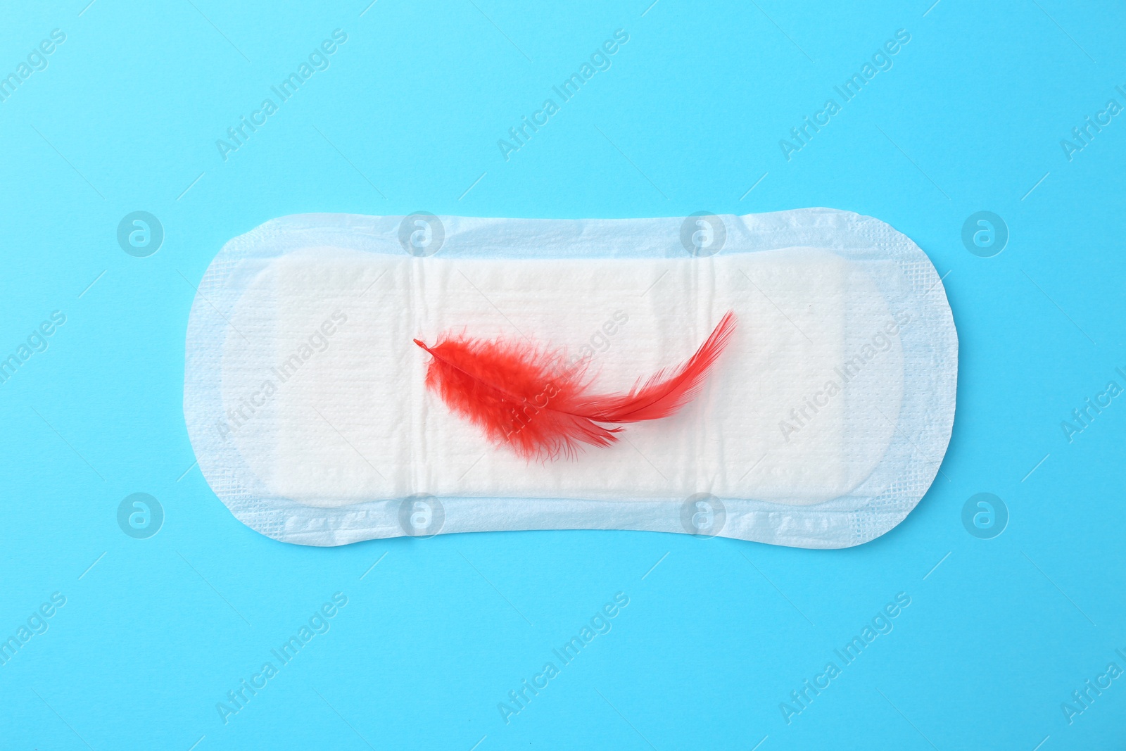 Photo of Menstrual pad with red feather on light blue background, top view