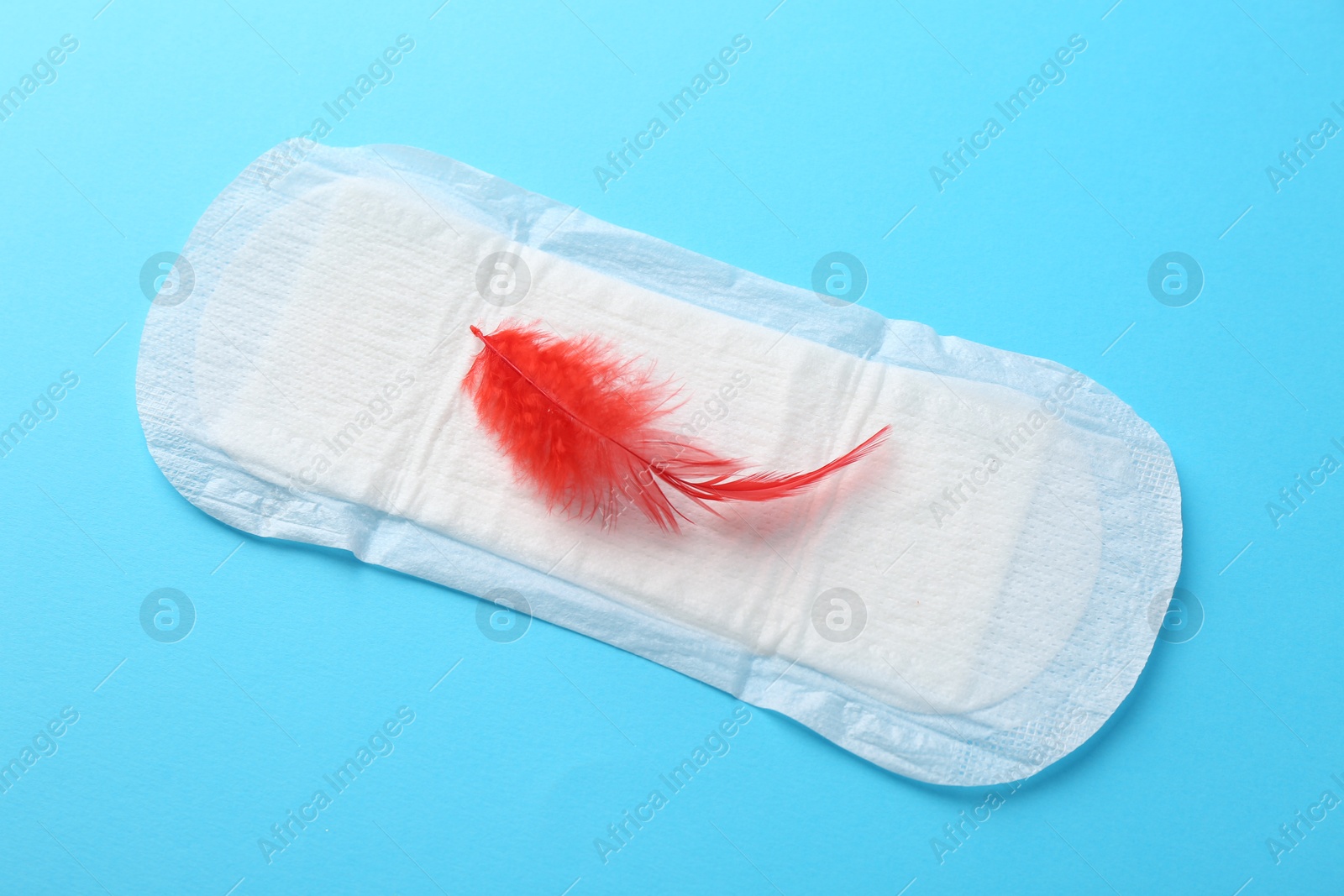 Photo of Menstrual pad with red feather on light blue background, top view