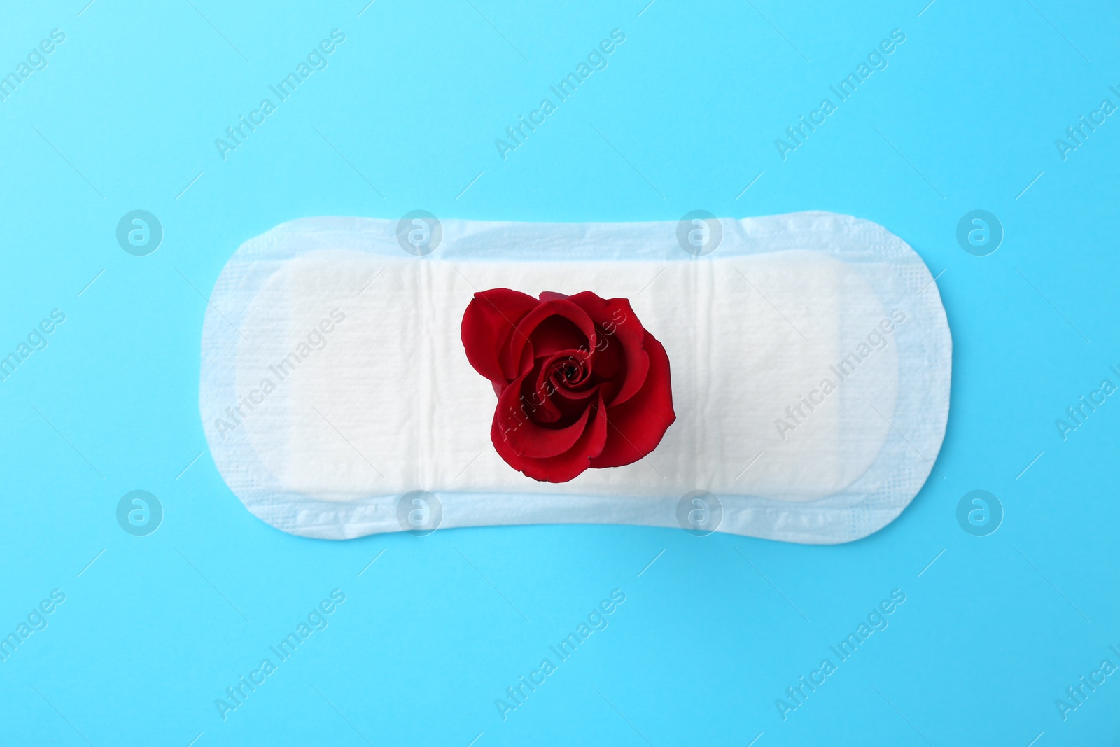 Photo of Menstrual pad with red flower on light blue background, top view