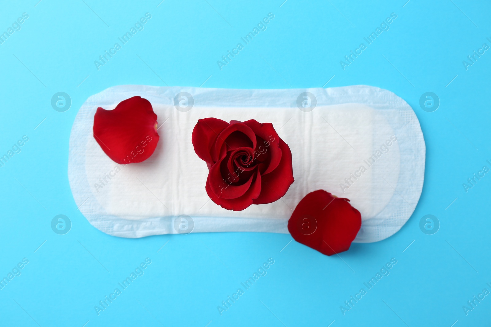 Photo of Menstrual pad with red flower on light blue background, top view