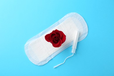 Photo of Menstrual pad with red flower and tampon on light blue background, top view