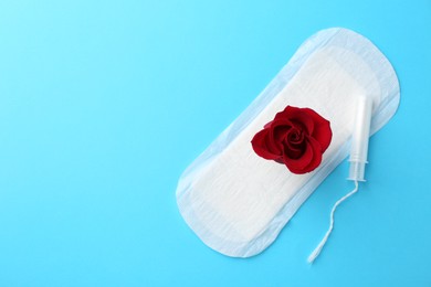 Photo of Menstrual pad with red flower and tampon on light blue background, top view. Space for text