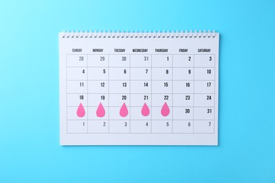 Photo of Menstruation. Calendar with marked dates on light blue background, top view