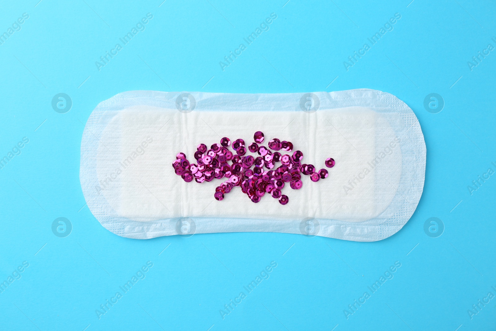 Photo of Menstrual pad and sequins on light blue background, top view