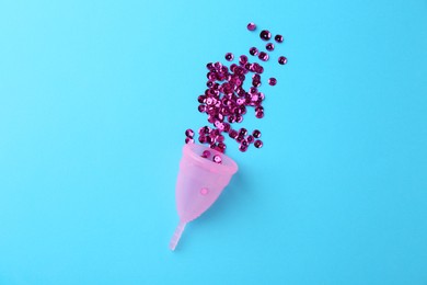 Menstrual cup and sequins on light blue background, top view