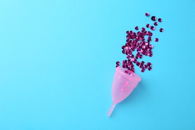 Photo of Menstrual cup and sequins on light blue background, top view. Space for text