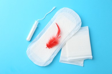 Photo of Menstrual pad with red feather and tampon on light blue background, top view