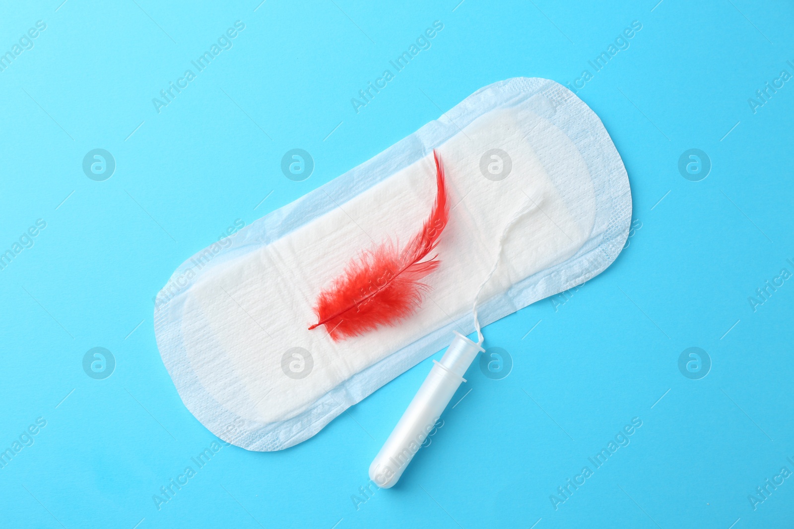 Photo of Menstrual pad with red feather and tampon on light blue background, top view