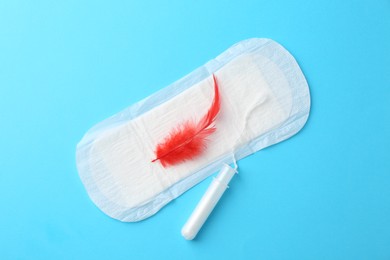 Menstrual pad with red feather and tampon on light blue background, top view