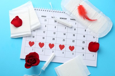 Photo of Flat lay composition with calendar and menstrual products on light blue background