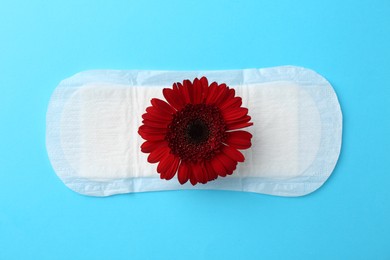 Photo of Menstrual pad with red flower on light blue background, top view