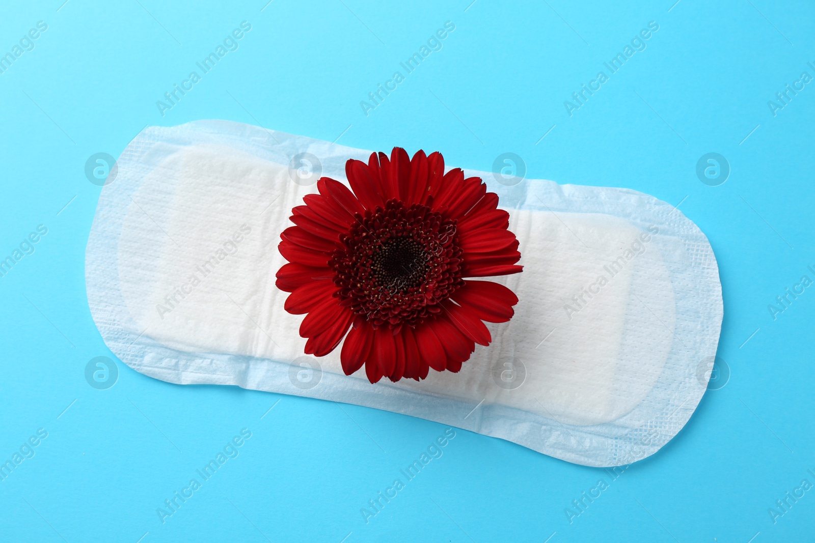 Photo of Menstrual pad with red flower on light blue background, top view