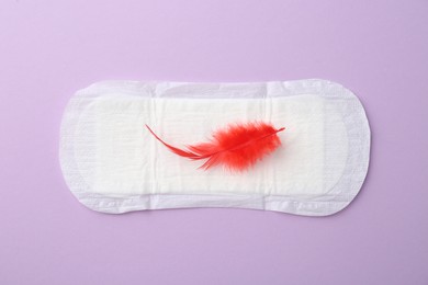 Photo of Menstrual pad with red feather on violet background, top view