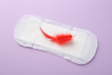 Photo of Menstrual pad with red feather on violet background, top view