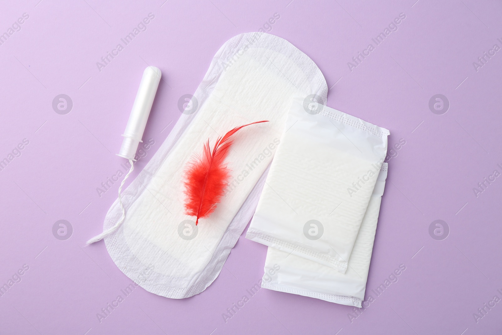 Photo of Menstrual pad with red feather and tampon on violet background, top view