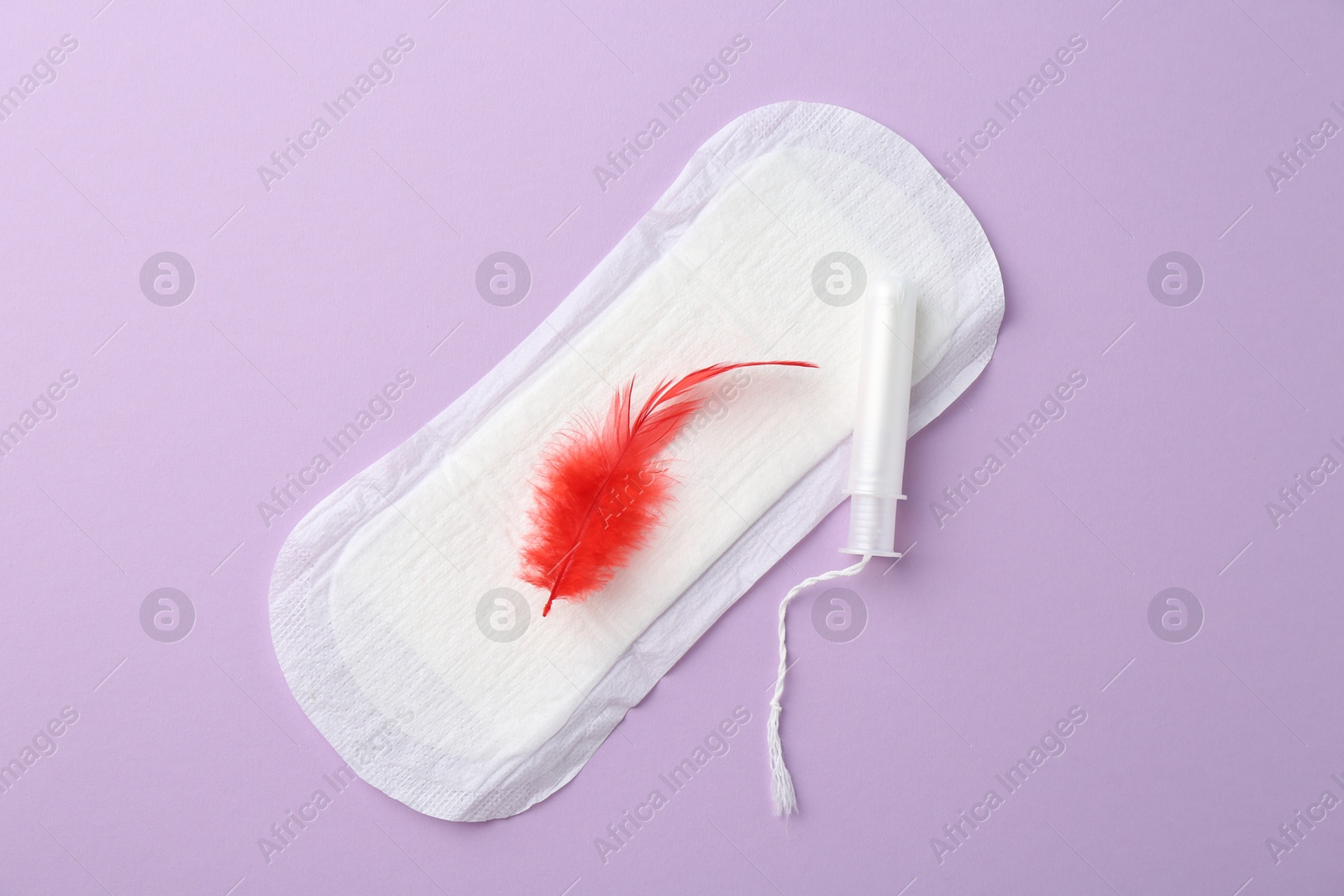 Photo of Menstrual pad with red feather and tampon on violet background, top view