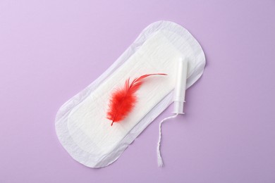 Photo of Menstrual pad with red feather and tampon on violet background, top view