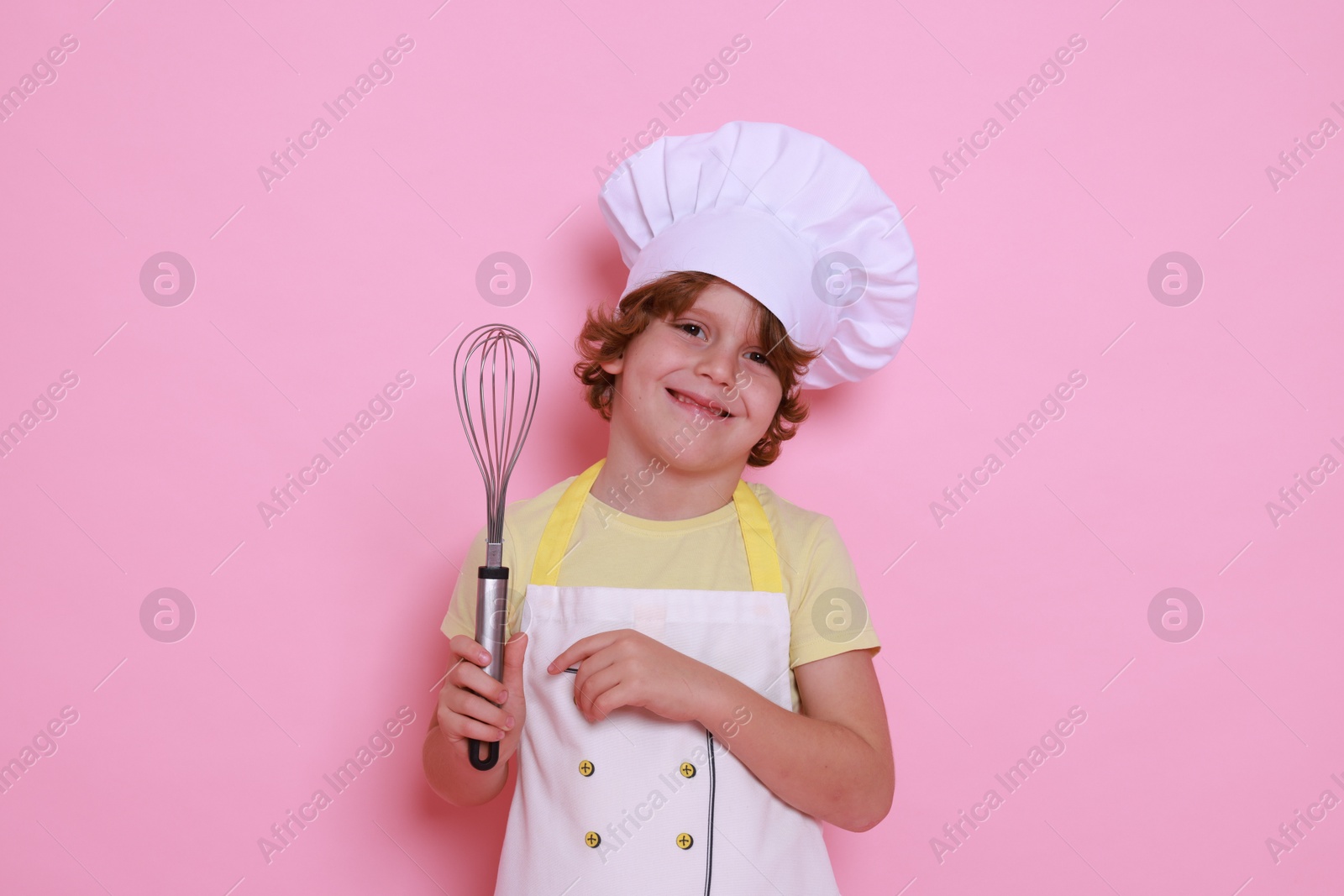 Photo of Little boy with whisk pretending to be chef on pink background. Dreaming about future profession