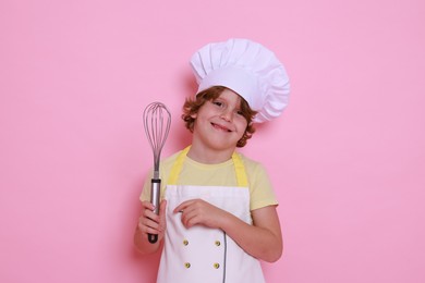 Little boy with whisk pretending to be chef on pink background. Dreaming about future profession