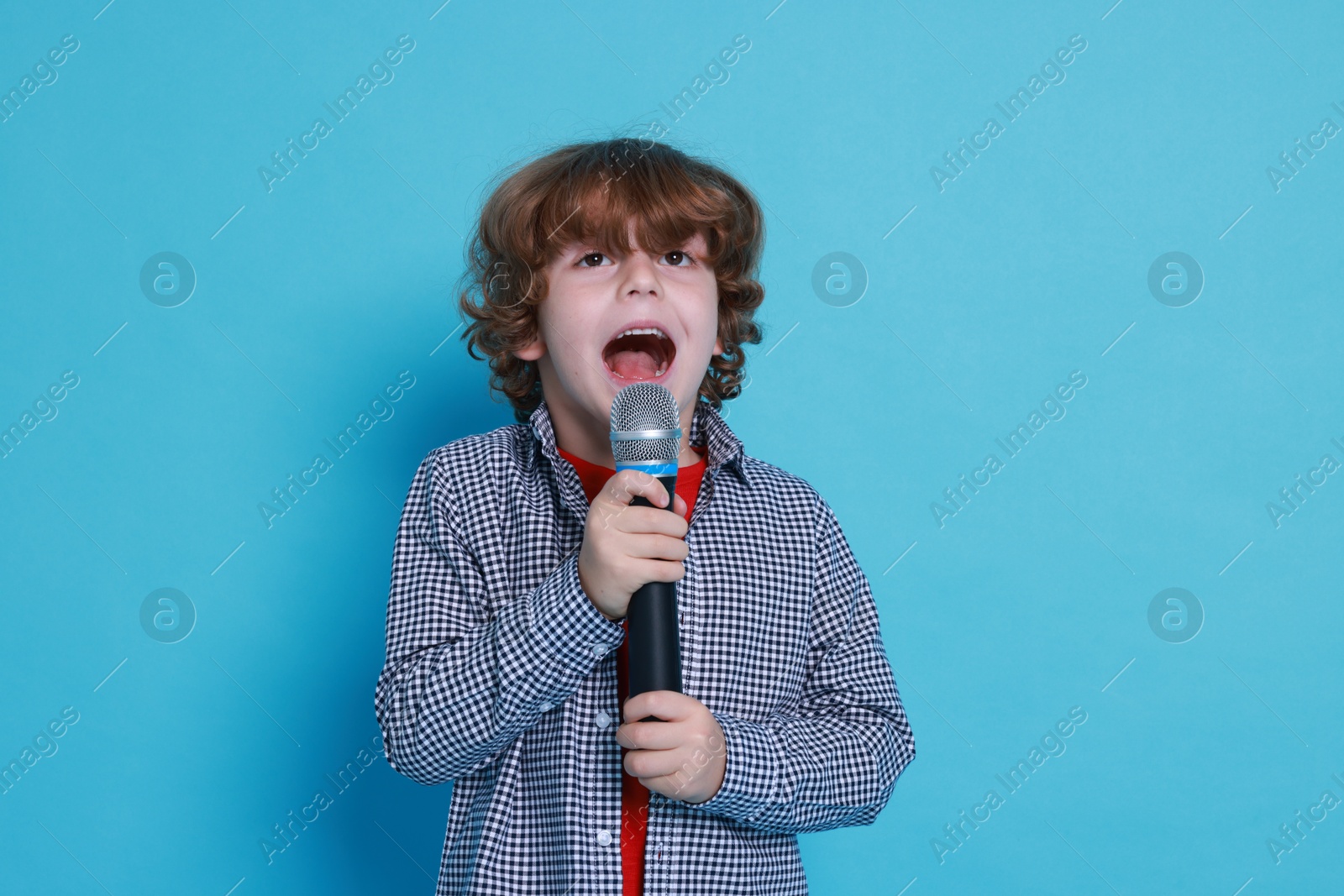 Photo of Little boy with microphone pretending to be singer on light blue background. Dreaming about future profession