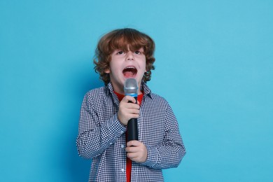 Little boy with microphone pretending to be singer on light blue background. Dreaming about future profession