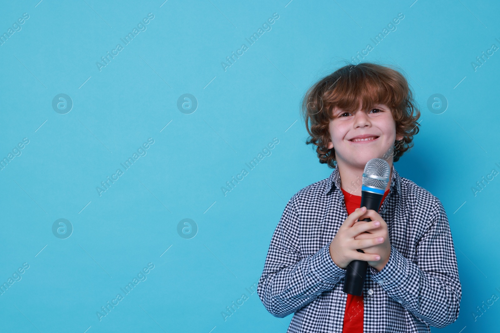 Photo of Little boy with microphone pretending to be singer on light blue background, space for text. Dreaming about future profession