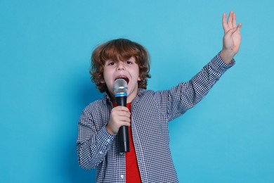 Photo of Little boy with microphone pretending to be singer on light blue background. Dreaming about future profession