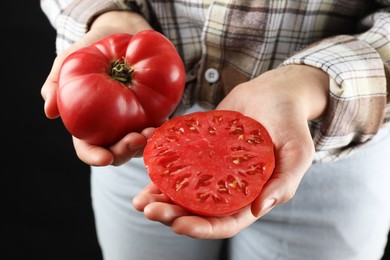 Photo of Woman holding whole and cut ripe tomatoes on black background, closeup