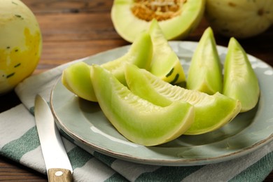 Photo of Plate with pieces of honeydew melon and knife on wooden table, closeup