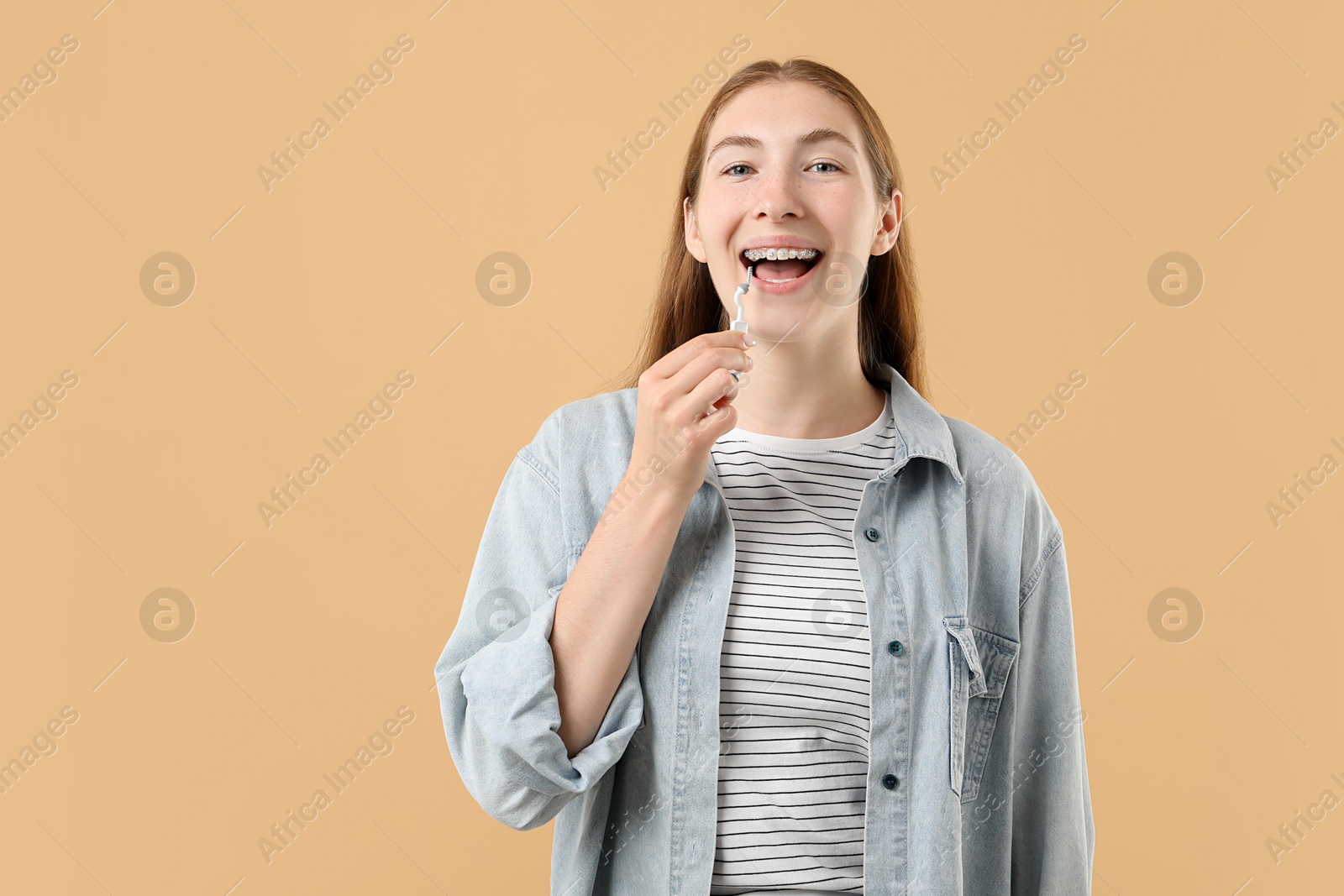 Photo of Girl with braces cleaning teeth with interdental brush on beige background