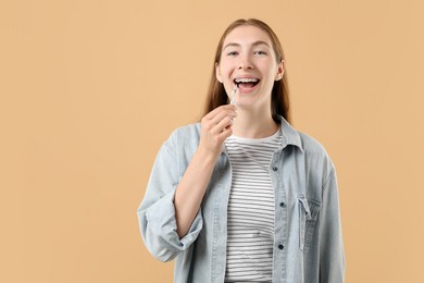 Photo of Girl with braces cleaning teeth with interdental brush on beige background