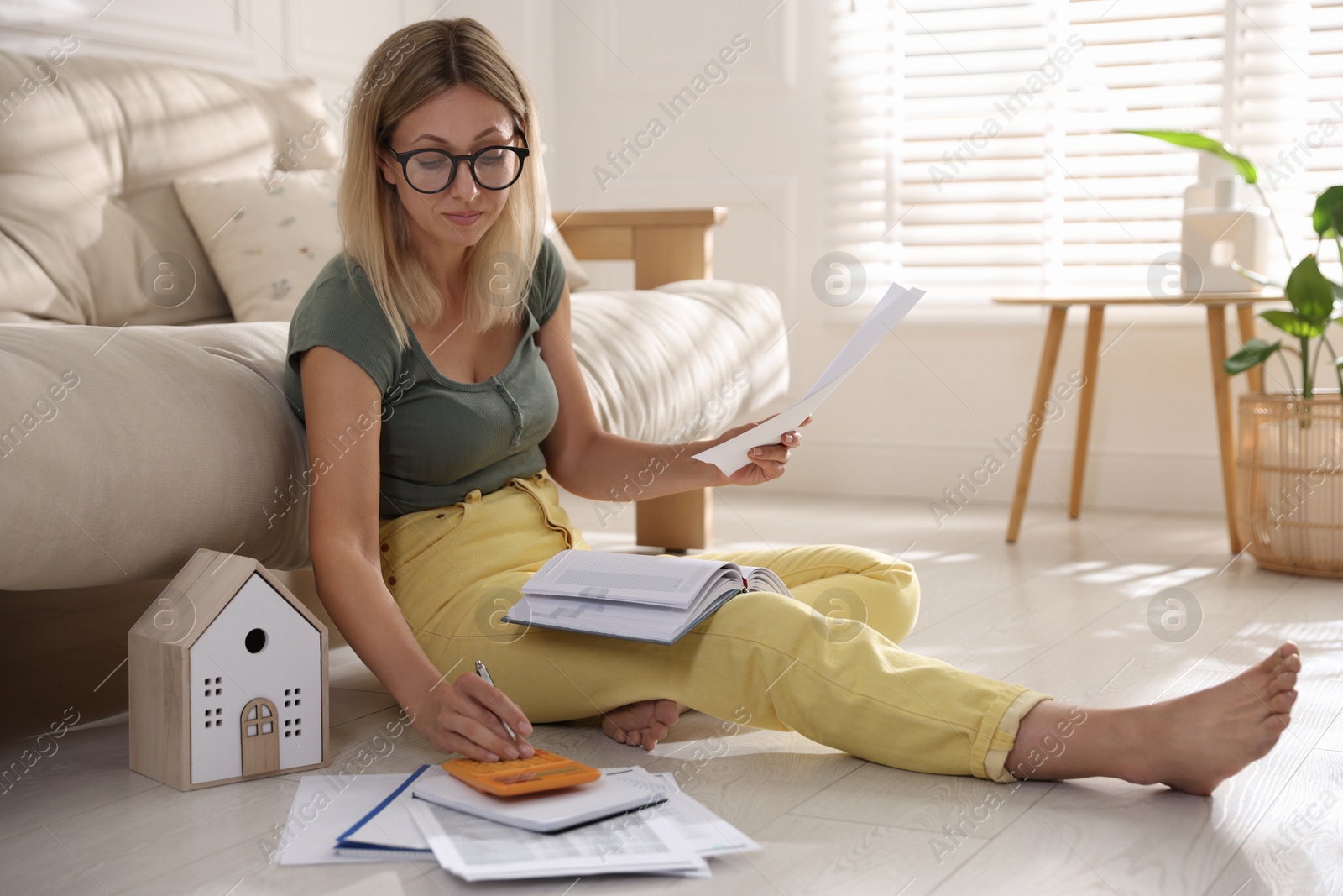 Photo of Budget planning. Woman using calculator while working with accounting documents on floor indoors