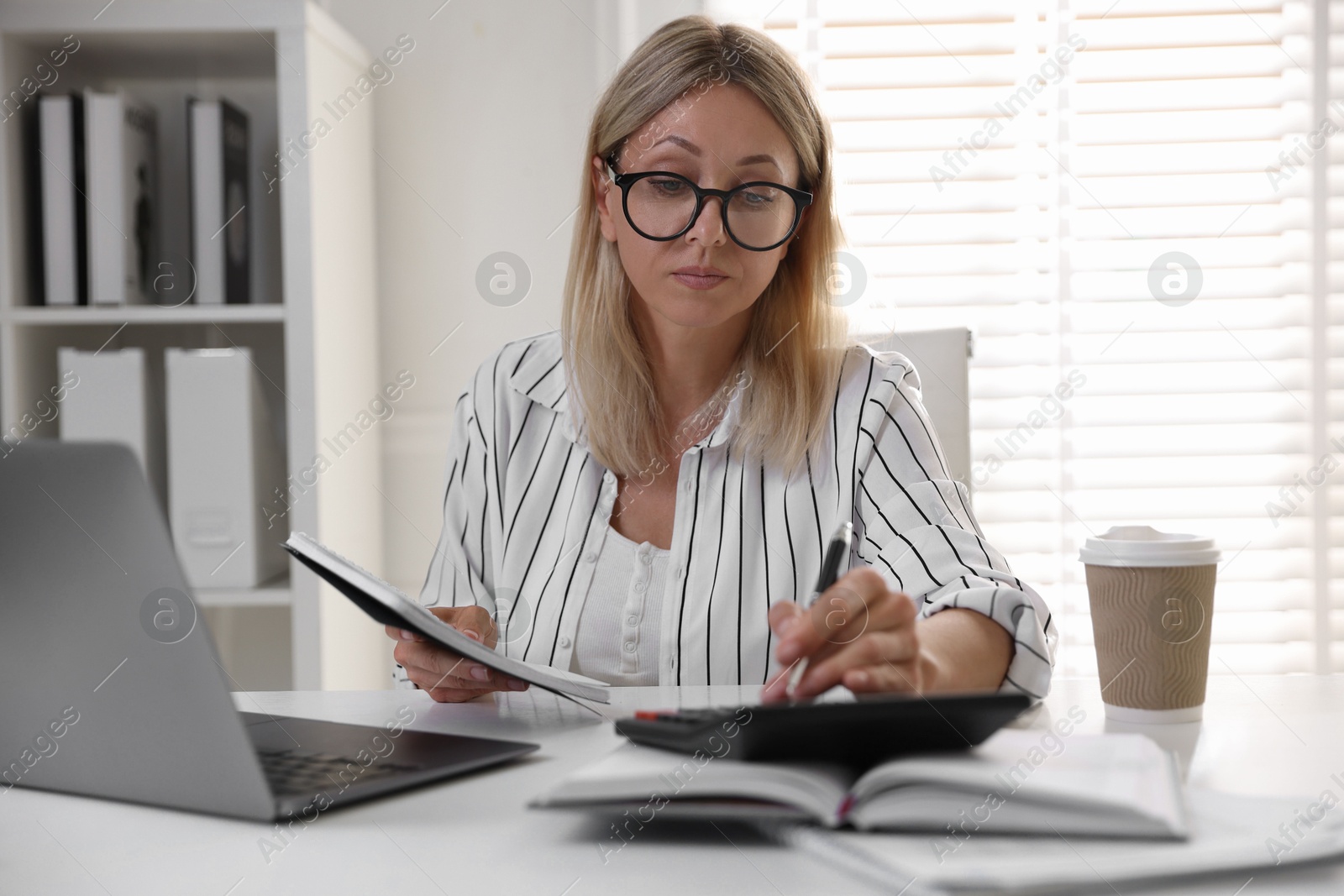 Photo of Budget planning. Woman with notebook using calculator at table indoors