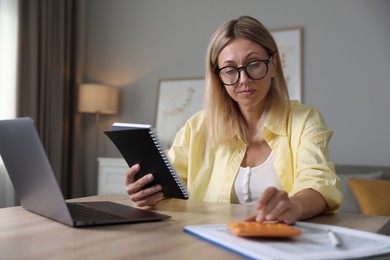 Budget planning. Woman with notebook using calculator at table indoors