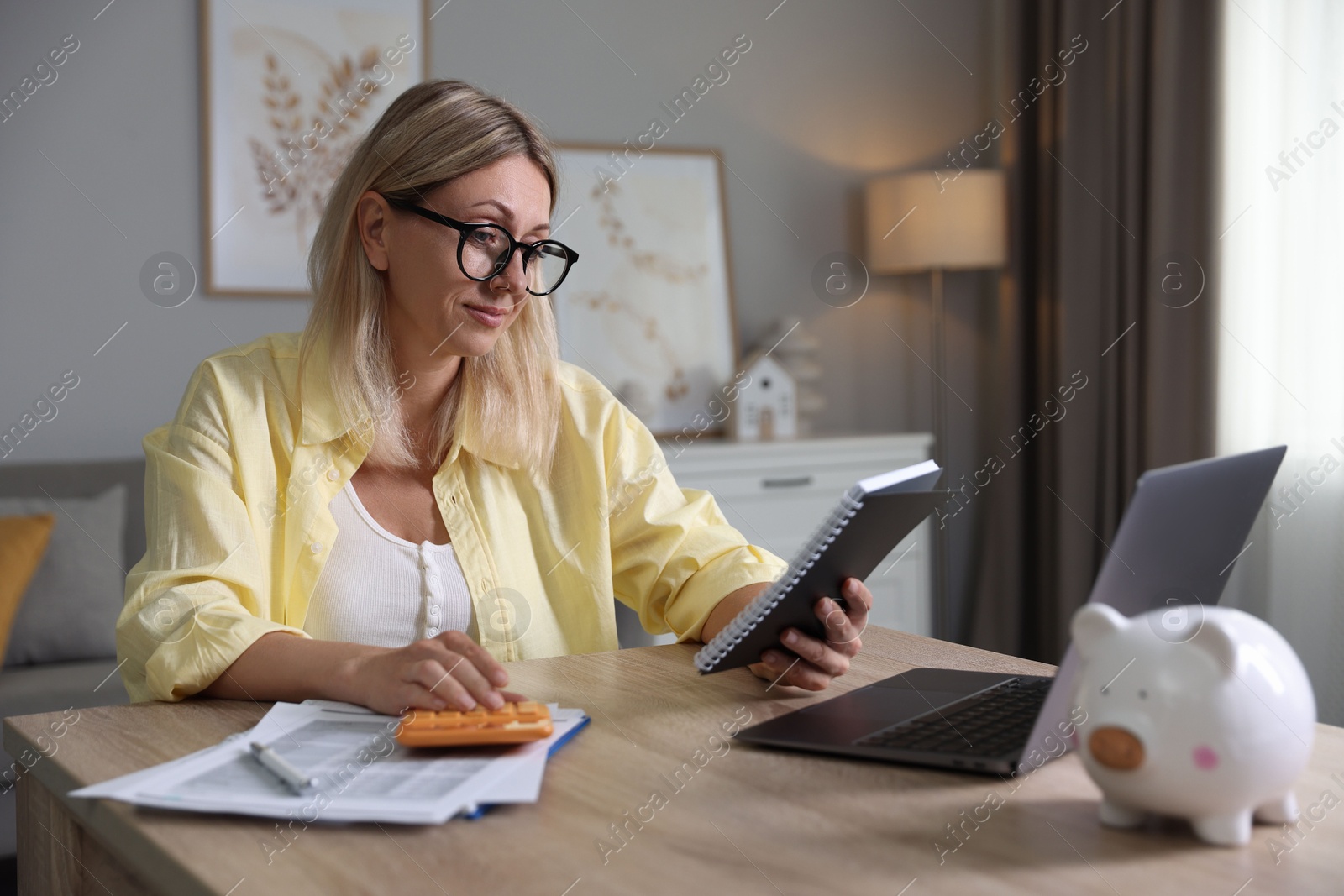 Photo of Budget planning. Woman with notebook using calculator at table indoors