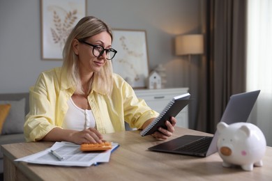 Budget planning. Woman with notebook using calculator at table indoors